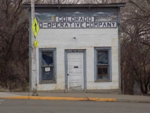 Small white brick building with a central door, two windows, and a sign reading "COLORADO CO-OPERATIVE COMPANY."