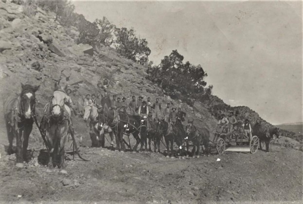 Group of people and horses on a rocky path beside a hillside with a horse-drawn wagon.