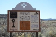 Informational sign in a desert landscape with a clear sky and distant mountains.