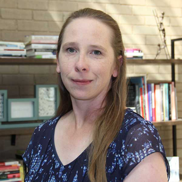 A close-up photo of Samantha Hager, Outreach and Digital Repository Librarian Colorado State Publications Library, a young woman with long brown hair and a blue top with books in the background.