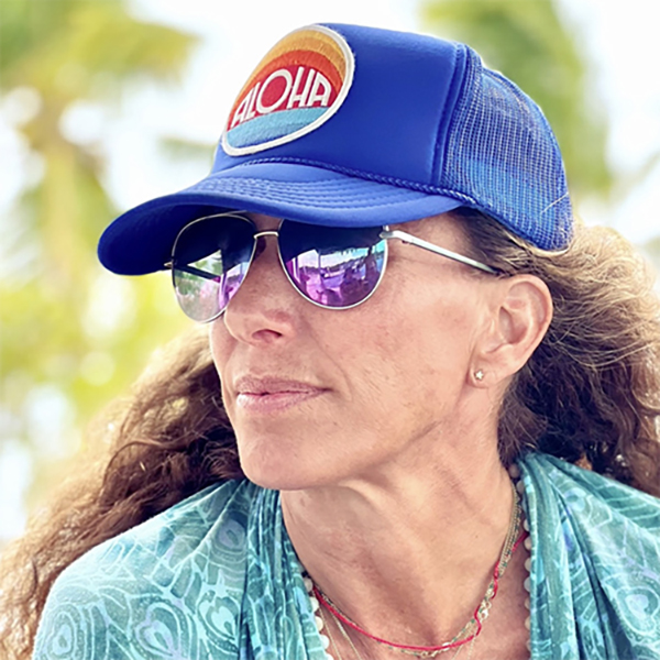 A close-up photo of Gabby Anstey McDonald, Outreach and Digital Repository Librarian Colorado State Publications Library, a young woman outside in warm weather wearing a blue baseball hat and sunglasses with long brown hair and a turquoise shawl.