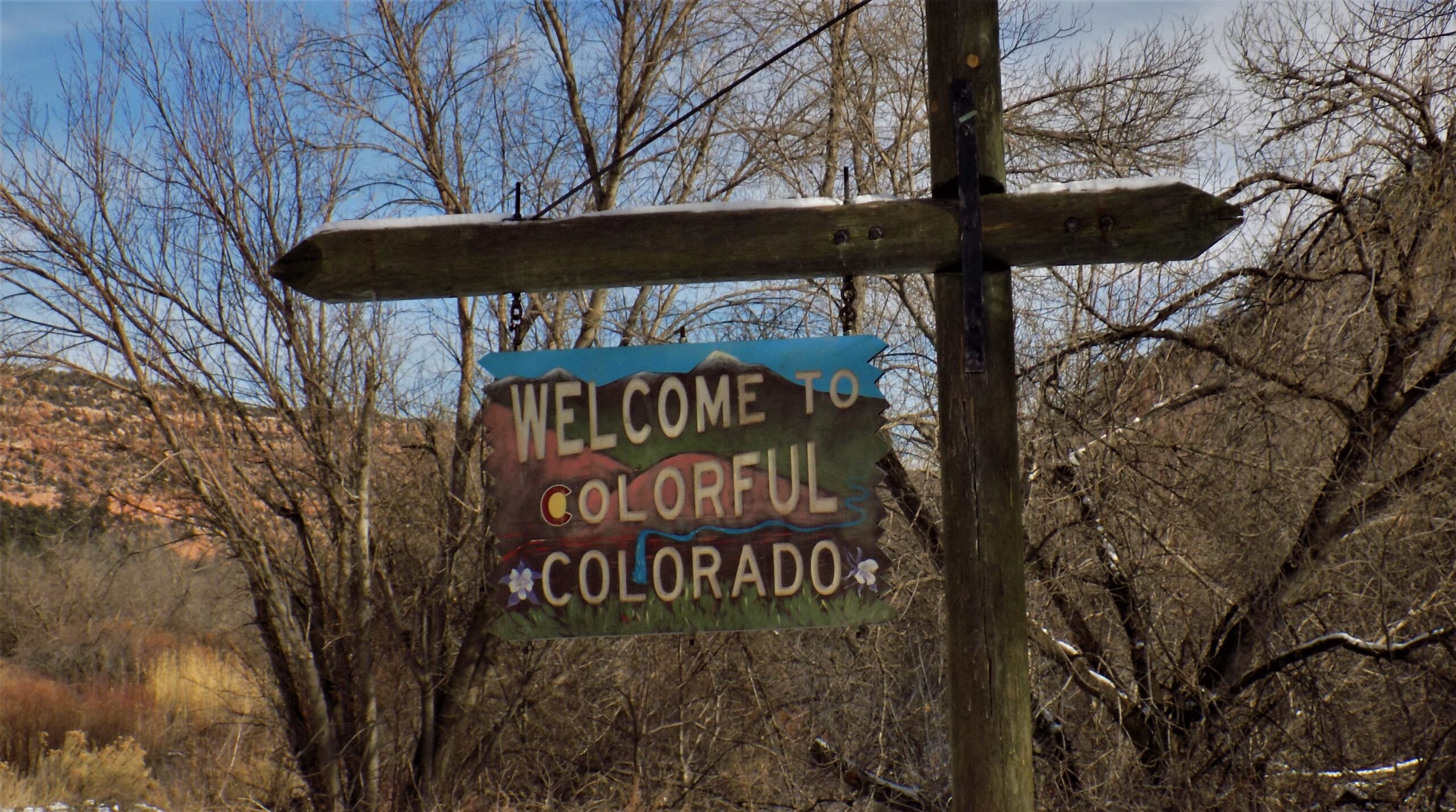 A wooden sign reading "Welcome to Colorful Colorado" against a backdrop of bare trees.